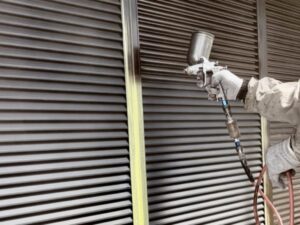 スプレーガンで雨戸の表面に均一に塗っている様子